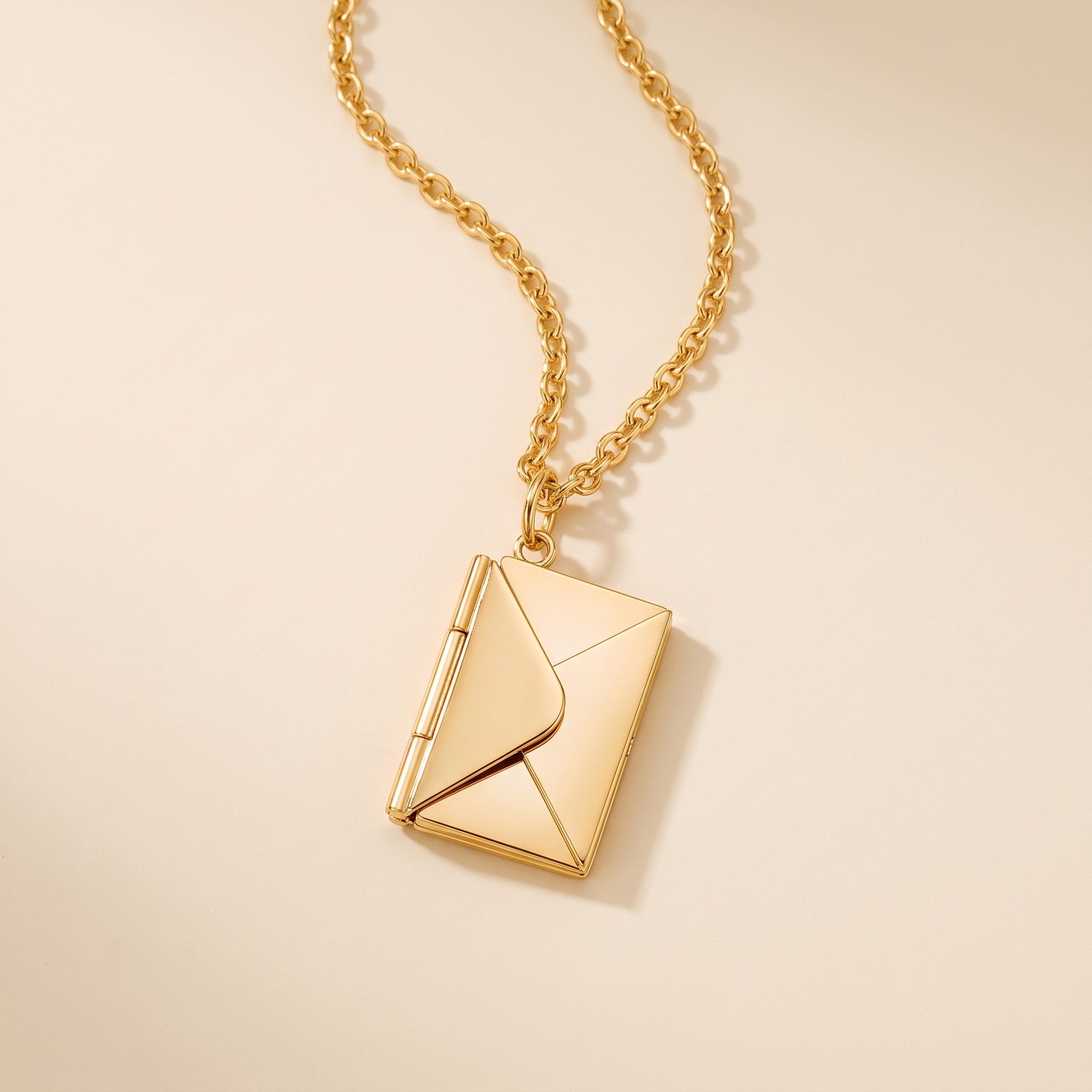 Gold envelope locket necklace on a cream background