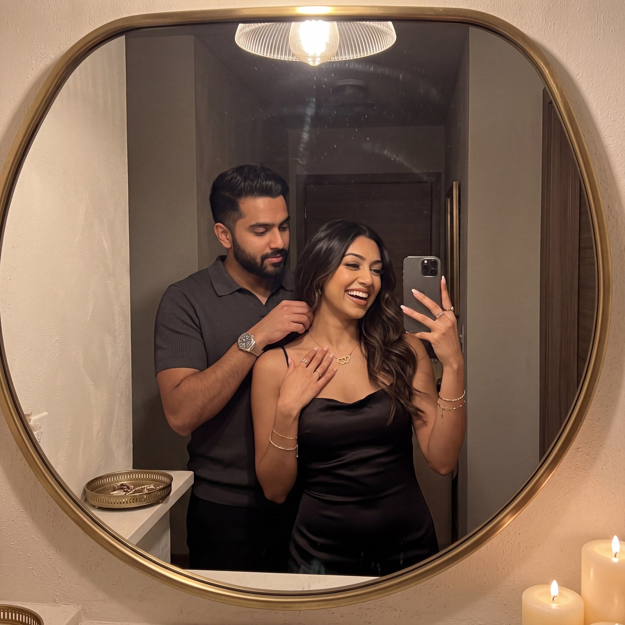 A couple's mirror selfie as he fastens her gold interlocked hearts necklace
